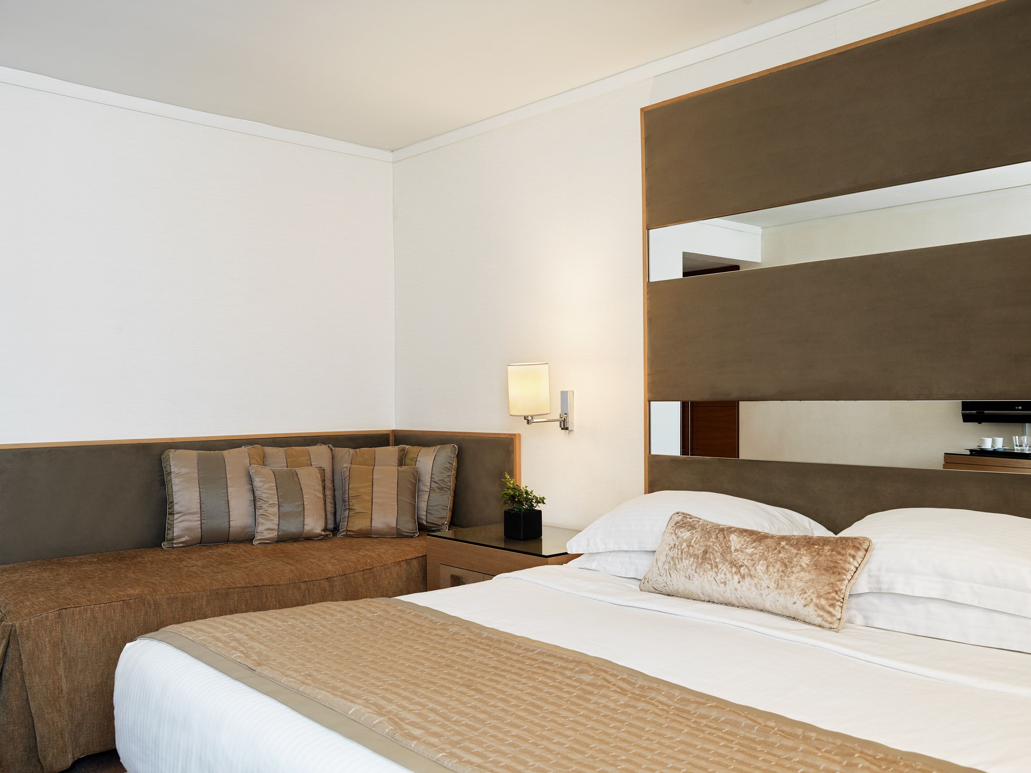 Een hotelkamer met een groot bed, een bank, een nachtkastje met een lamp en een grote spiegel boven het bed.