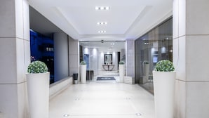 A modern hotel lobby with a clean, tiled floor, large potted plants, and a reception desk in the center. - Galaxy Hotel Iraklio (Heraklion)