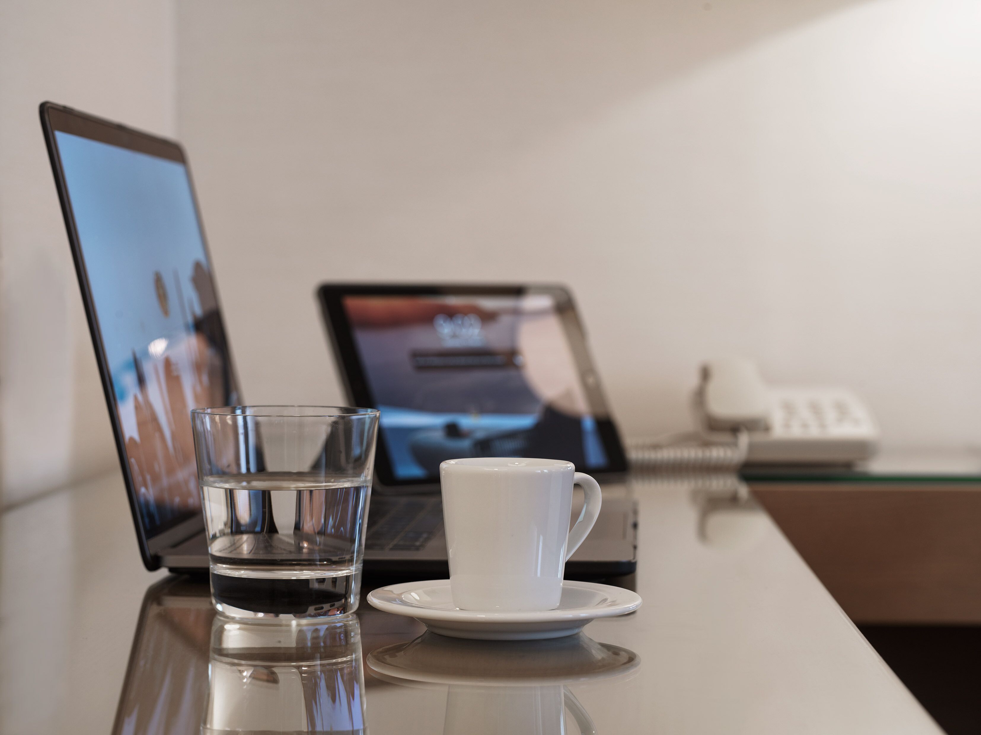 A laptop, a glass of water, and a white cup on a reflective surface.