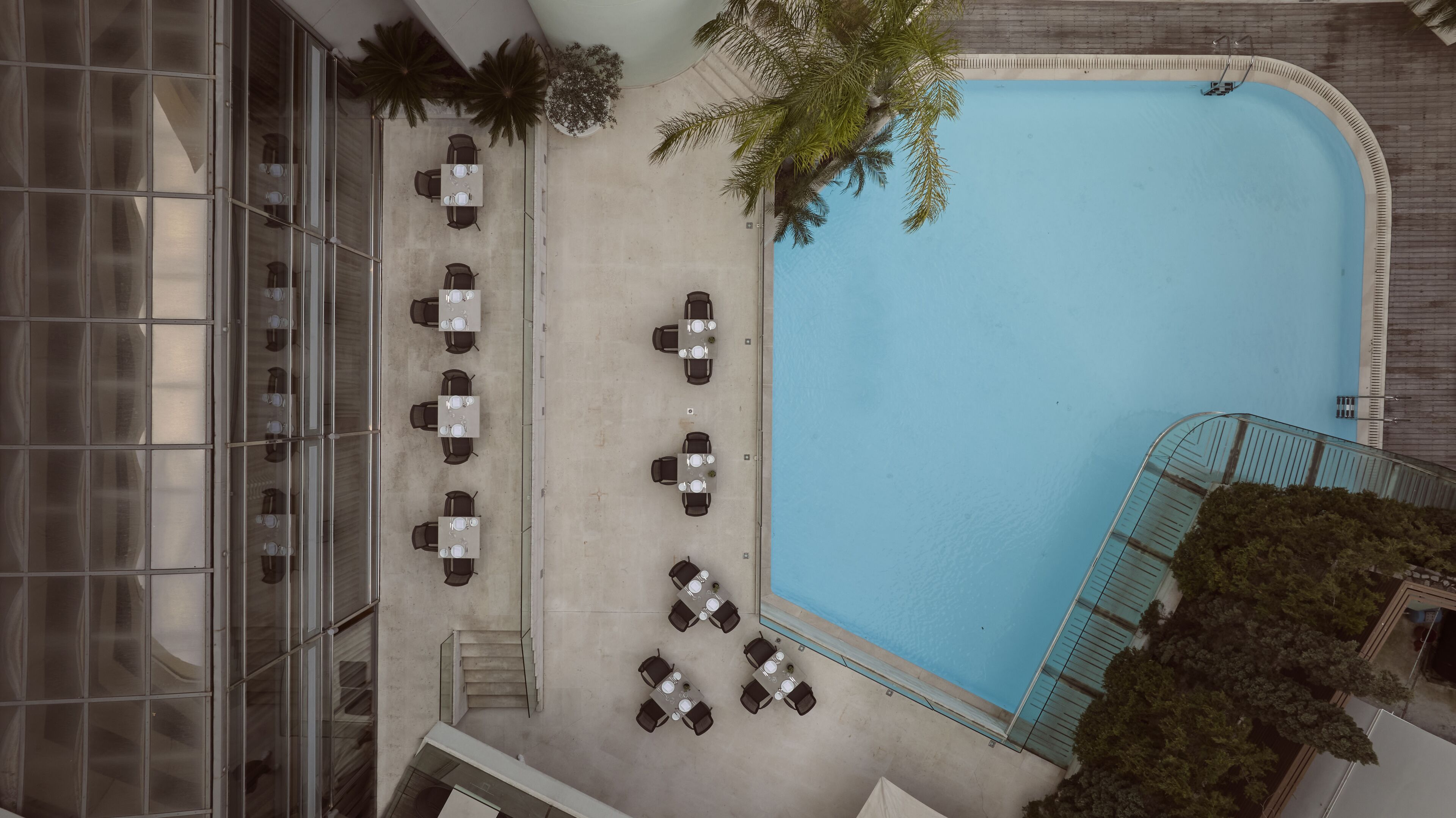 An aerial view of a hotel with a swimming pool, outdoor seating area, and a staircase leading to the pool.
