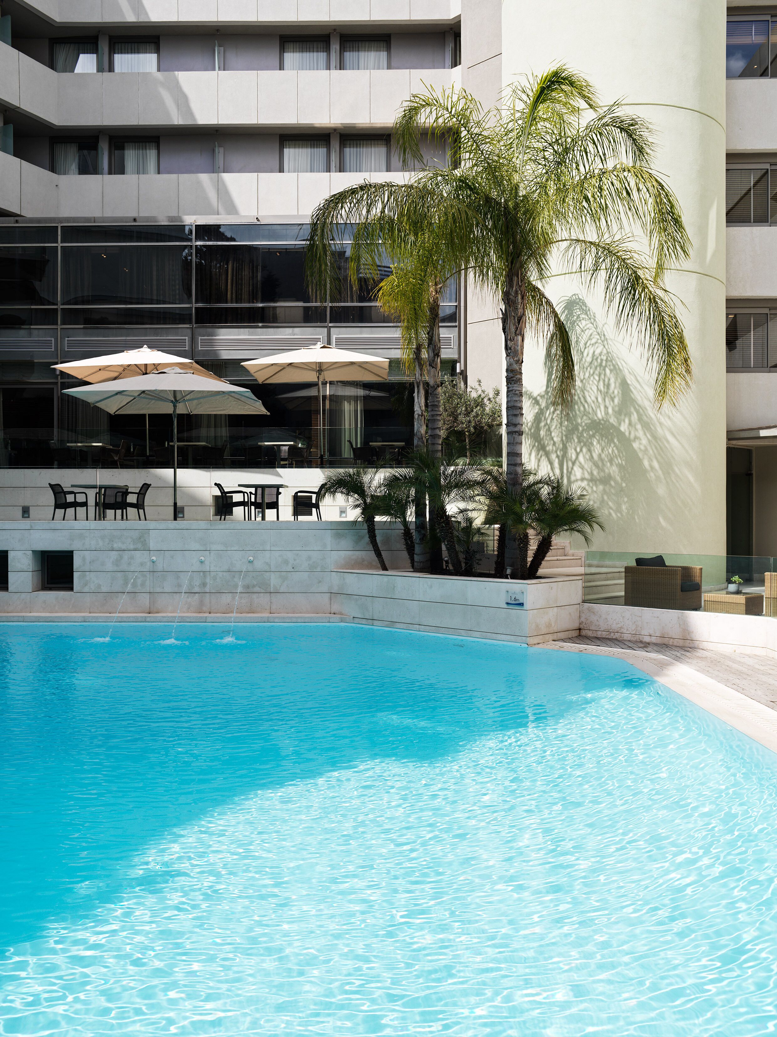 A swimming pool with a clear blue water surface, surrounded by a modern building with balconies and outdoor seating.