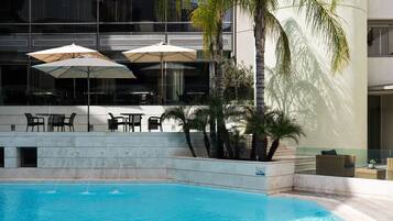A swimming pool with a clear blue water surface, surrounded by a modern building with balconies and outdoor seating.