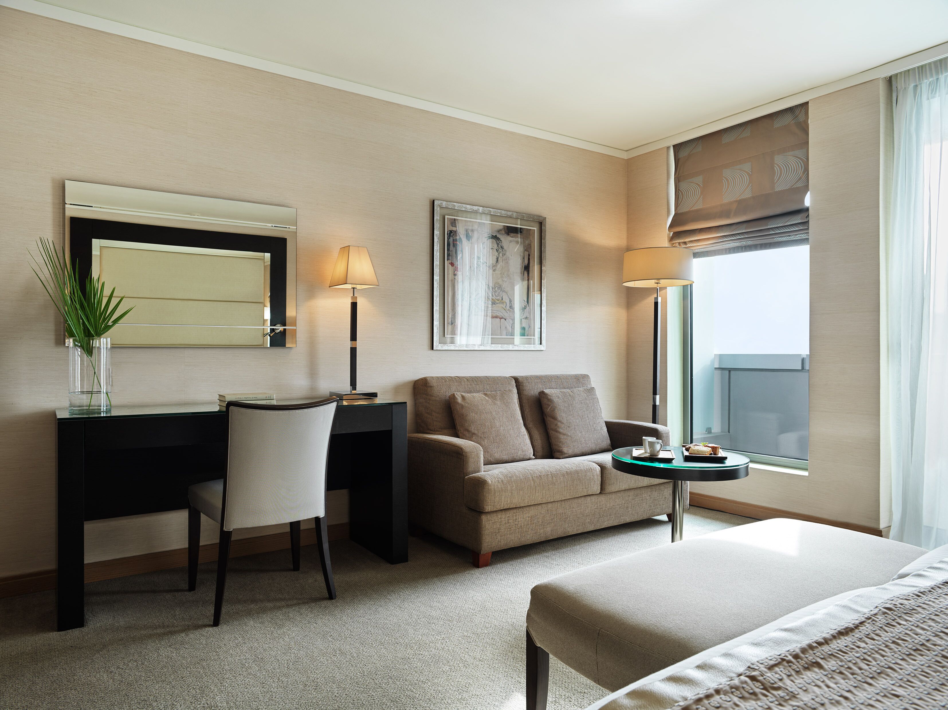 A hotel room with a desk, chair, sofa, and a bed.
