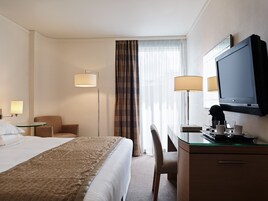Habitación de hotel con una cama, un escritorio con computadora, una silla, televisor y lámpara.