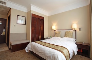 Una habitación de hotel con una cama grande, un banco, un armario de madera y dos lámparas de pared.
