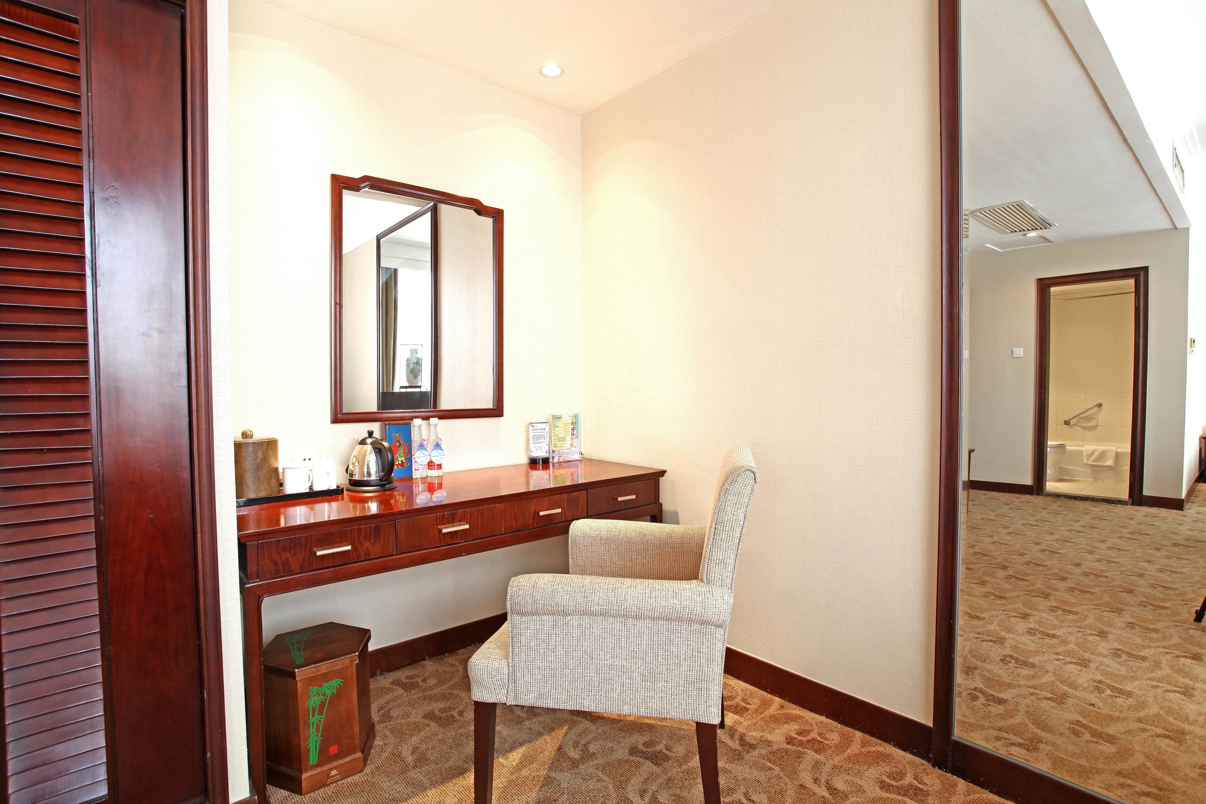A hotel room with a wooden desk, a chair, a large mirror, and a carpeted floor.