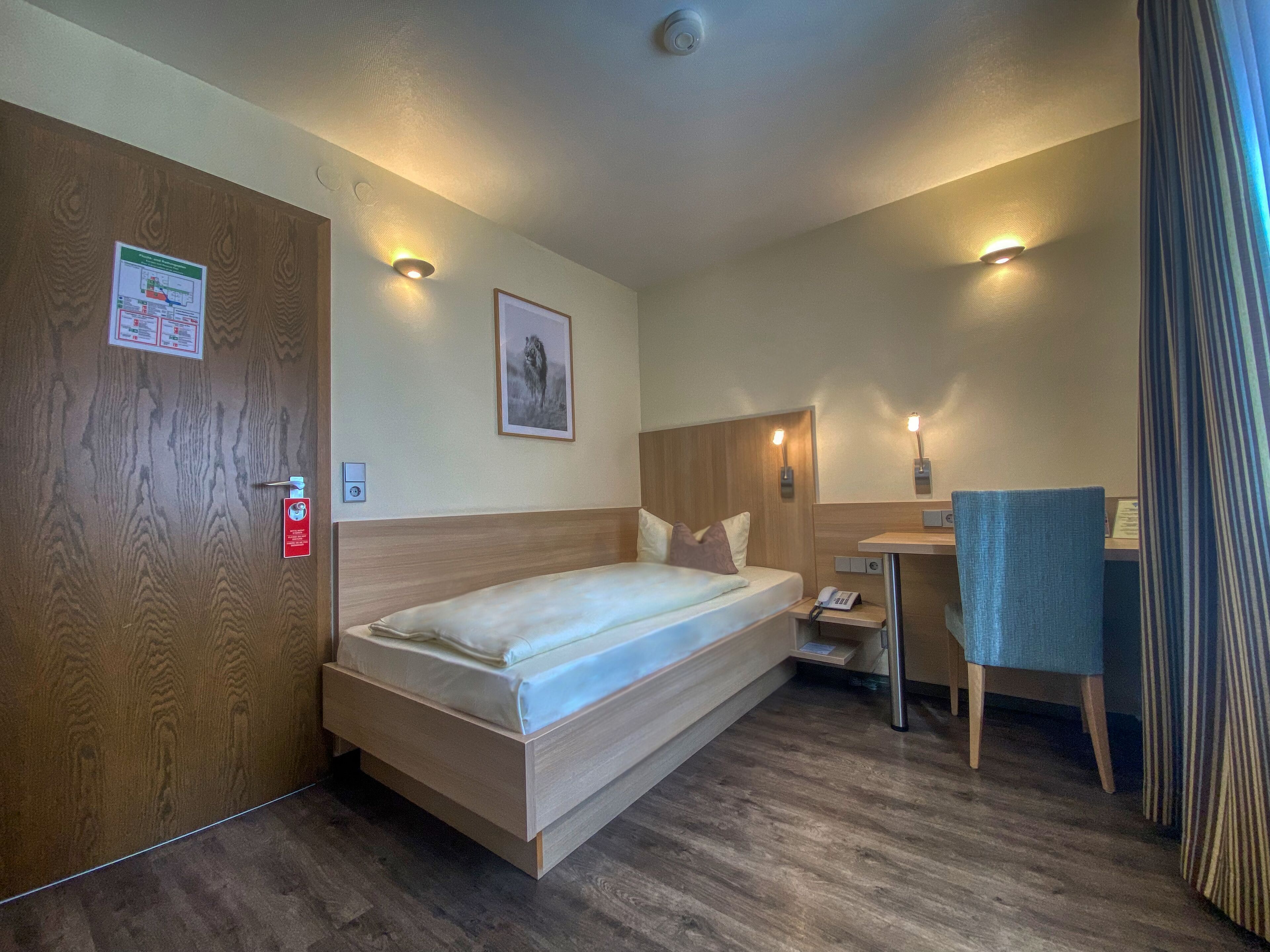 Habitación de hotel con cama de madera, un escritorio con silla, teléfono y un cuadro en la pared.