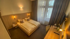 Camera d'albergo con un letto matrimoniale, comodini, una scrivania con sedia, una macchina per il caffè e una finestra con tende.
