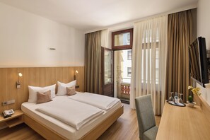 A hotel room with a large bed, a desk, a chair, a TV, and a window with curtains. - City Partner Hotel Berliner Hof (Karlsruhe)