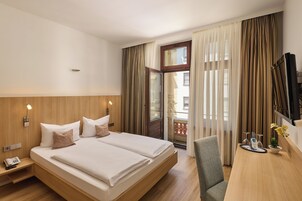 Quarto de hotel com cama grande, escrivaninha, cadeira, televisão e janela com cortinas.