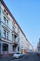 Un edificio histórico con detalles arquitectónicos ornamentales, una entrada visible y una vista de la calle con coches estacionados.