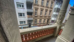 Un balcone con un muro in mattoni, una ringhiera in metallo e vista su un edificio con numerose finestre e balconi.