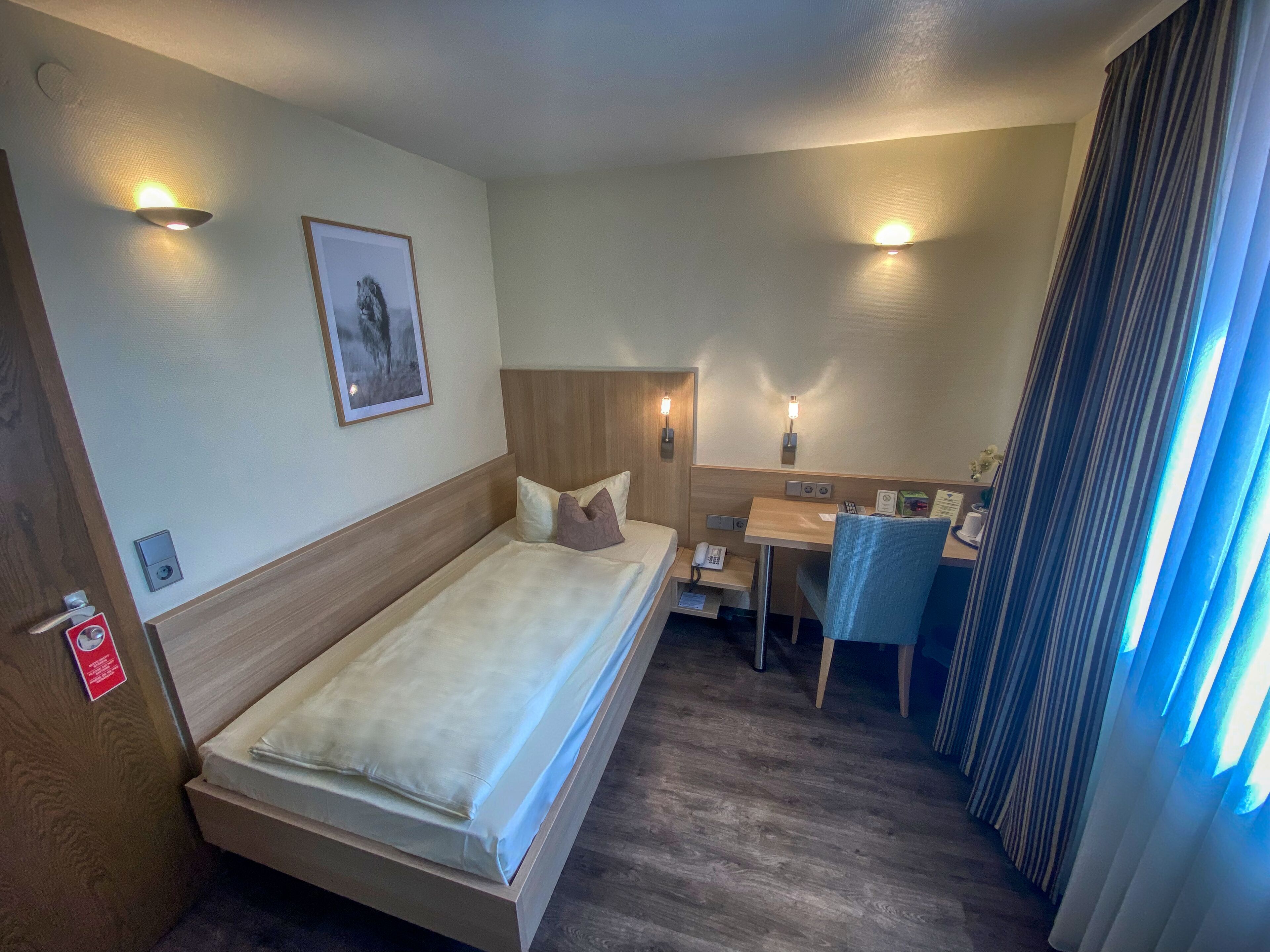 A hotel room with a bed, bedside table, desk, chair, and a small table with a telephone.