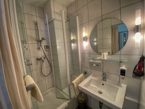 A modern bathroom with a glass shower enclosure, a white sink, and a mirror with lights. - City Partner Hotel Berliner Hof (Karlsruhe)