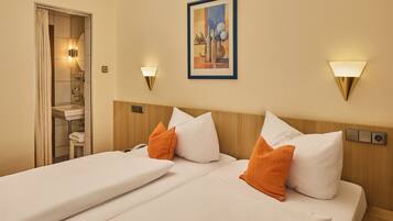 A hotel room with a bed, two pillows, a nightstand, a wall-mounted lamp, and a painting.