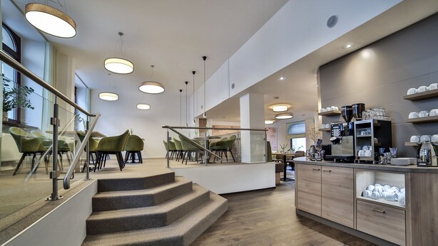 Un interno moderno con una scala che conduce a una zona relax, un bancone cucina con accessori per caffè e vista sull'esterno.