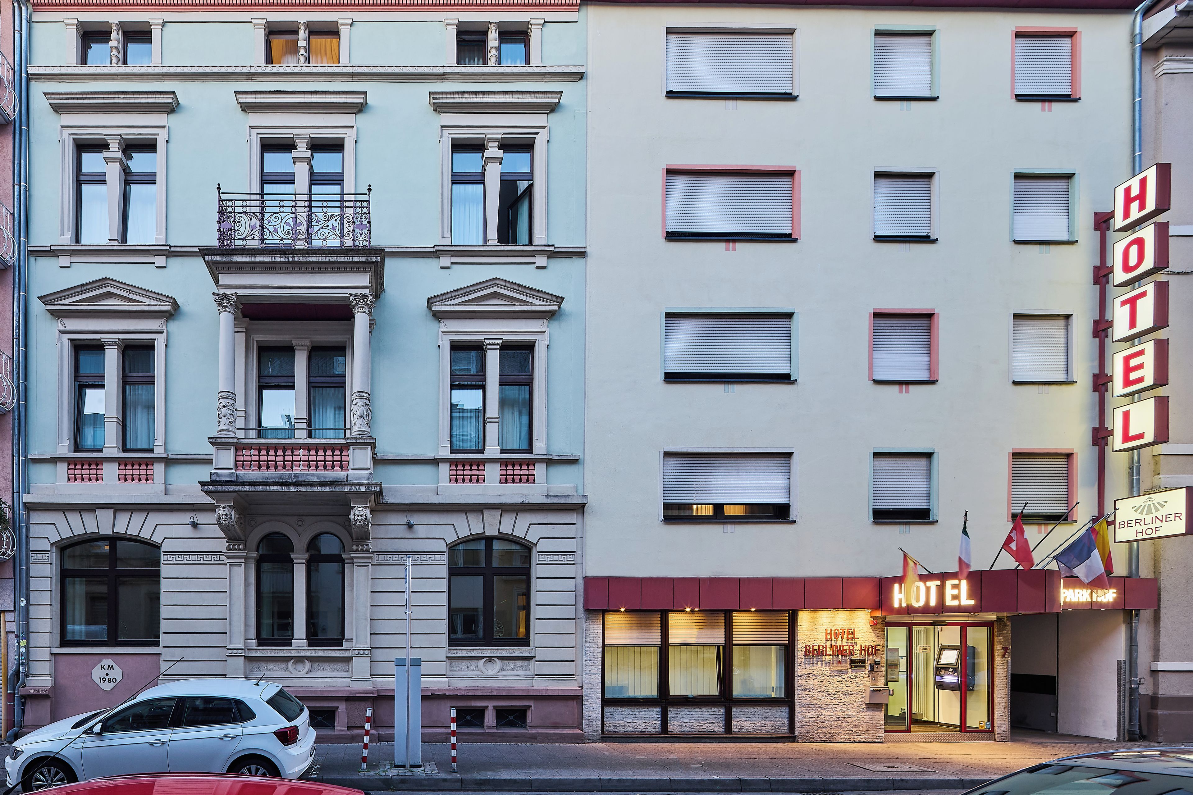 Fachada de hotel con varias ventanas, un letrero llamativo y un coche estacionado adelante.