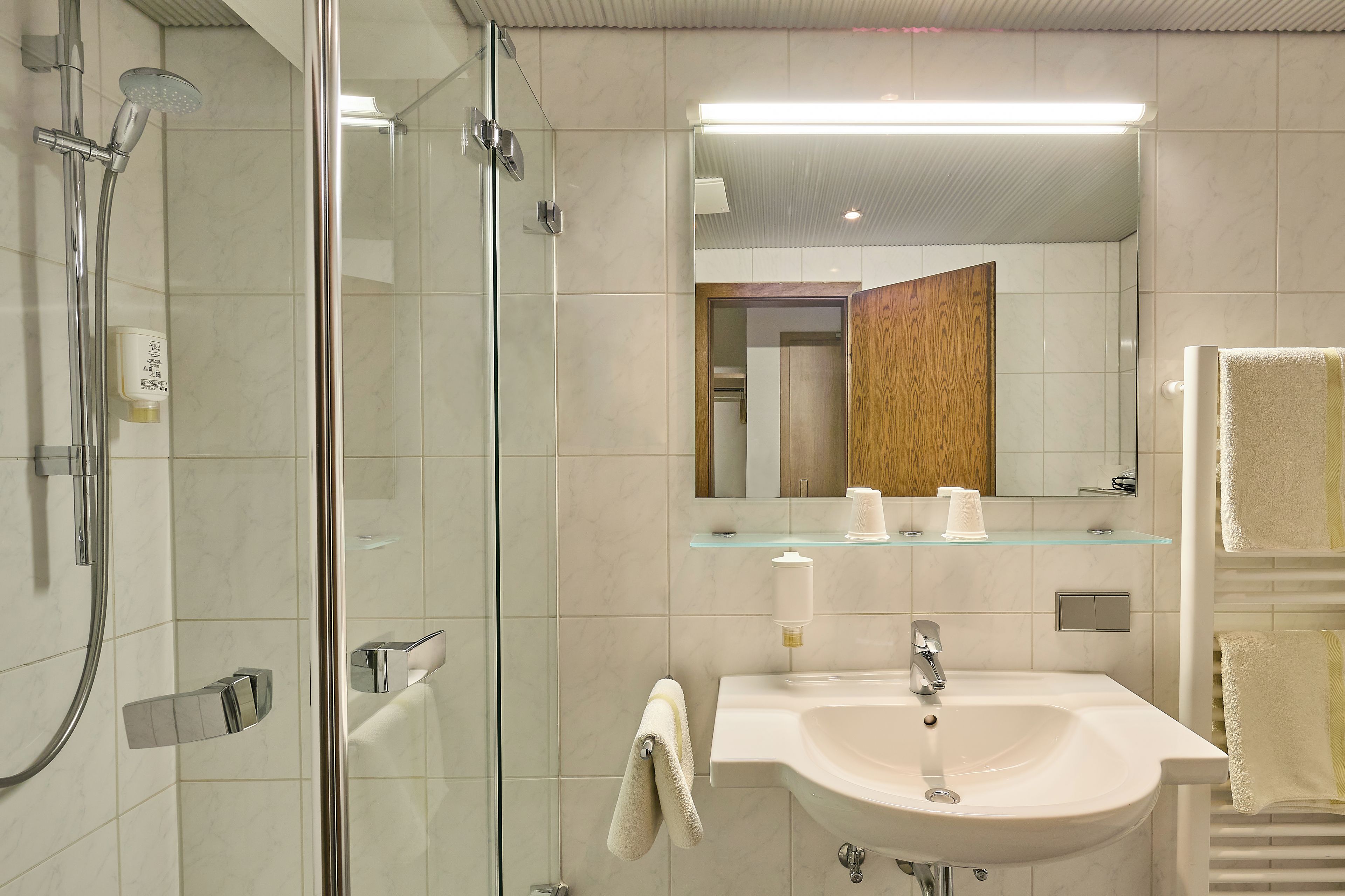 Ein modernes Badezimmer mit einer Duschkabine, einem Waschbecken mit Spiegel darüber und einem Handtuchhalter.