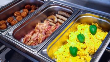 A buffet with various food options including scrambled eggs, bacon, sausages, and meatballs.