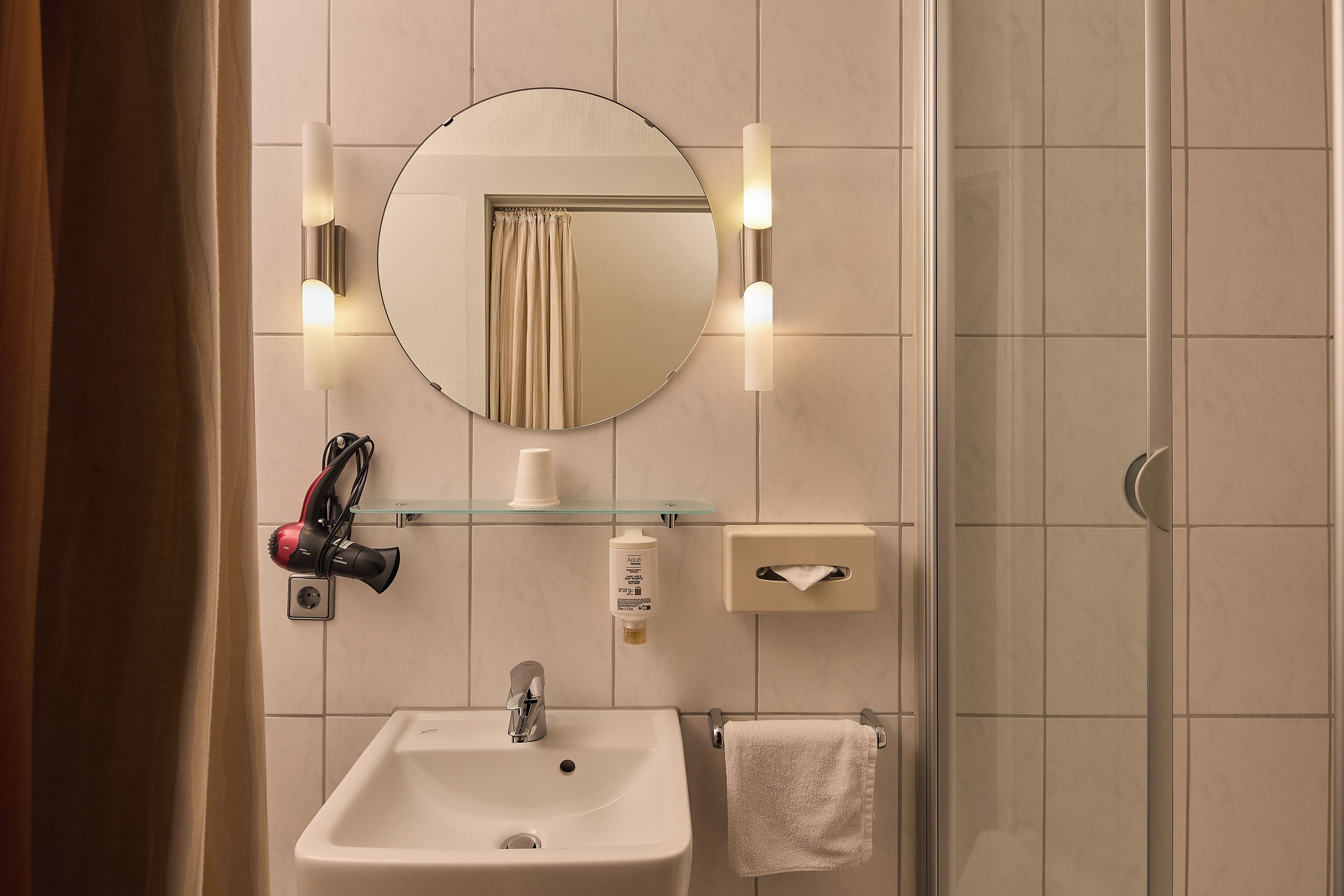Un baño con lavamanos, espejo, toallero y repisa de vidrio con una taza.