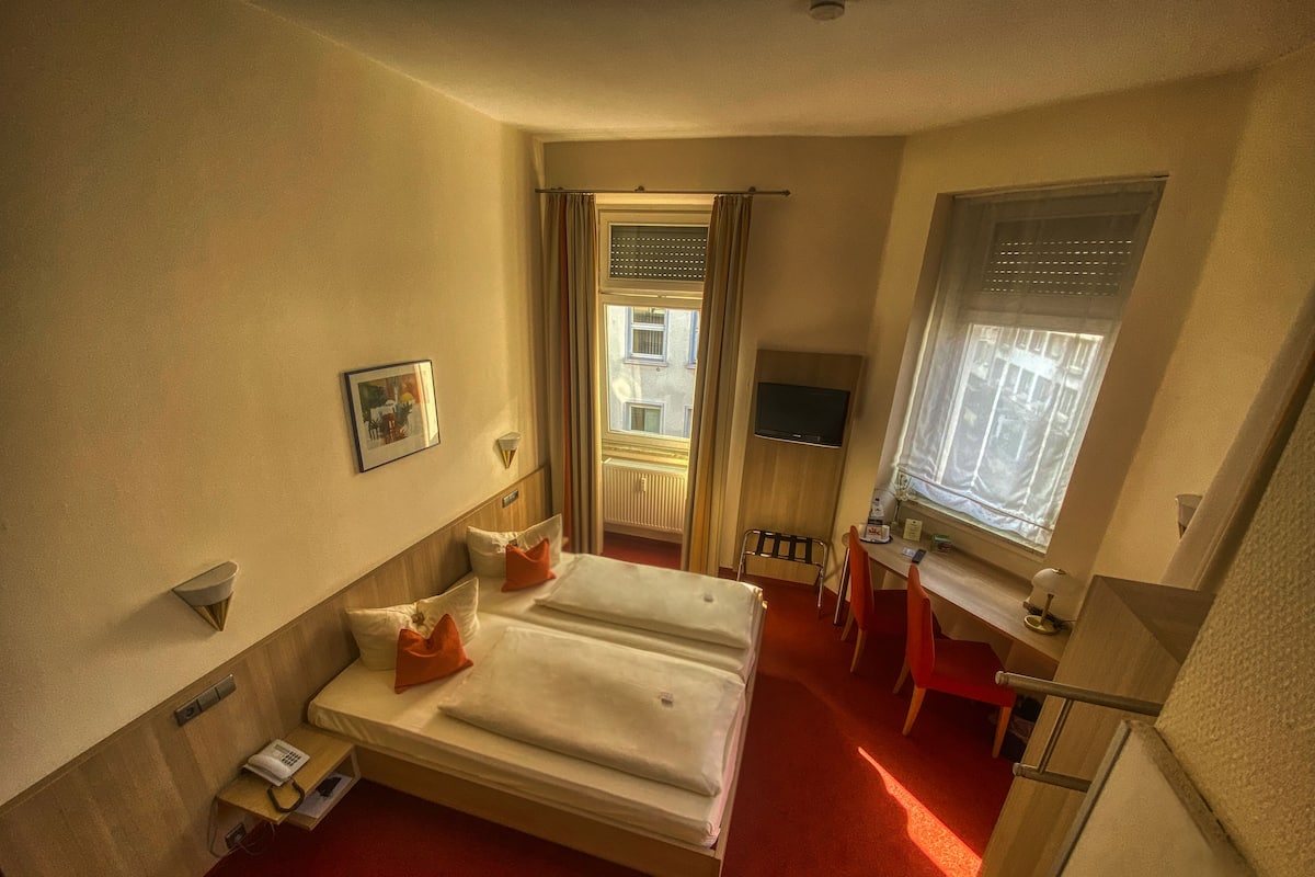 A hotel room with a bed, a desk, a chair, a TV, and a window.