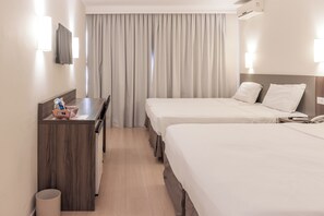 Una habitación de hotel con dos camas, un escritorio, un televisor y una ventana con cortinas.
