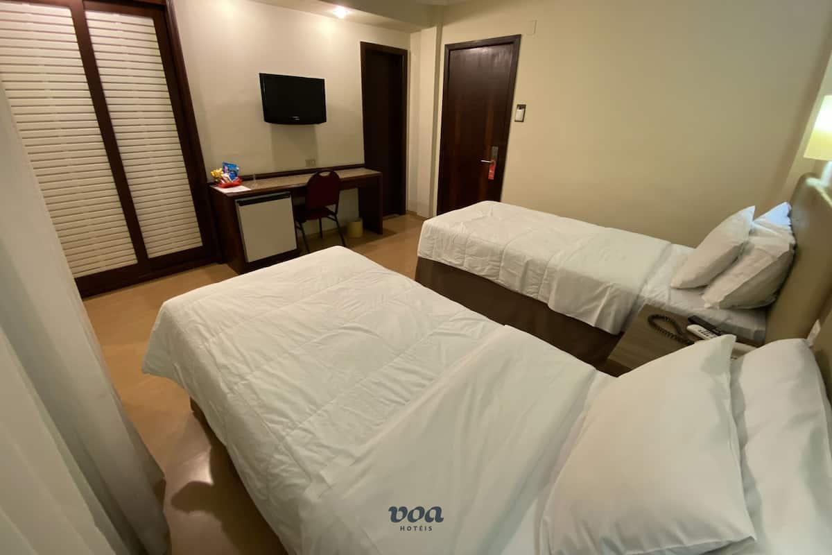 Una habitación de hotel con dos camas, un escritorio con silla, televisión y una puerta.
