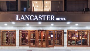 Das äußere Erscheinungsbild des Lancaster Hotels mit einem markanten Eingang, großen Fenstern und einer Schilder über den Türen.