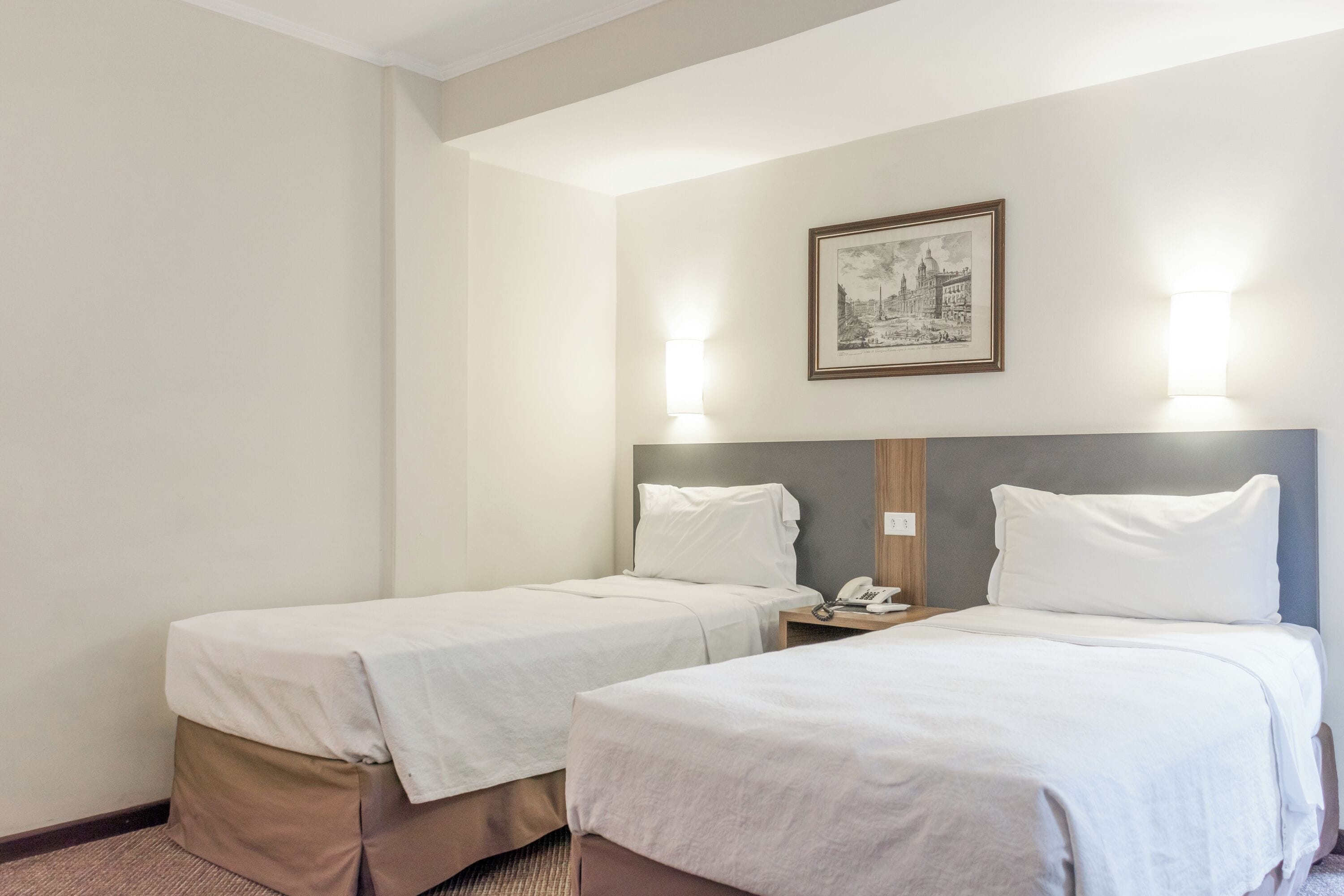 A hotel room with two single beds, a nightstand with a phone, and a framed picture on the wall.