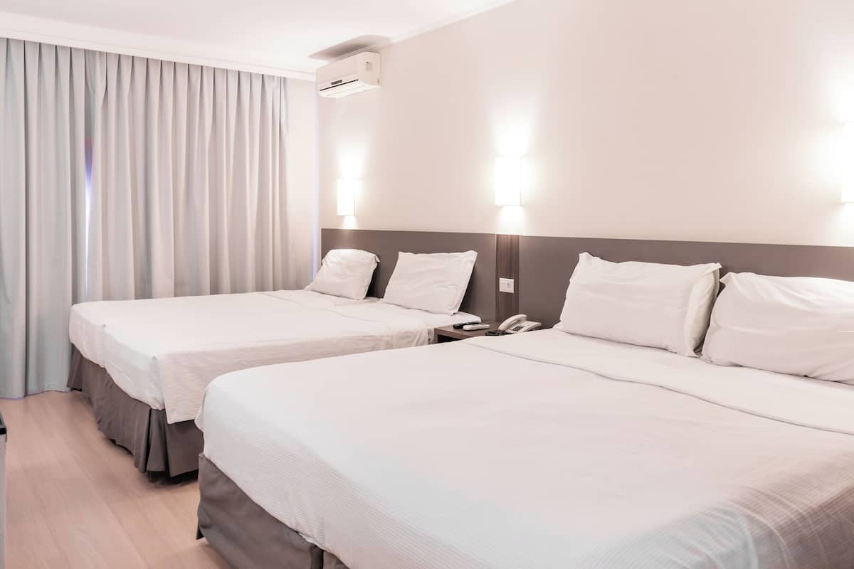 Habitación de hotel con dos camas, una mesita de noche con teléfono y aire acondicionado instalado en la pared.