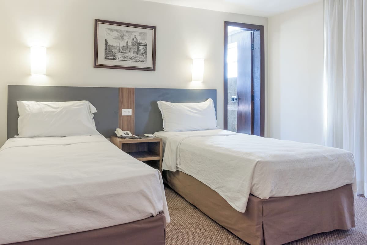 Una habitación de hotel con dos camas, una mesita de noche con un teléfono y un cuadro en la pared.