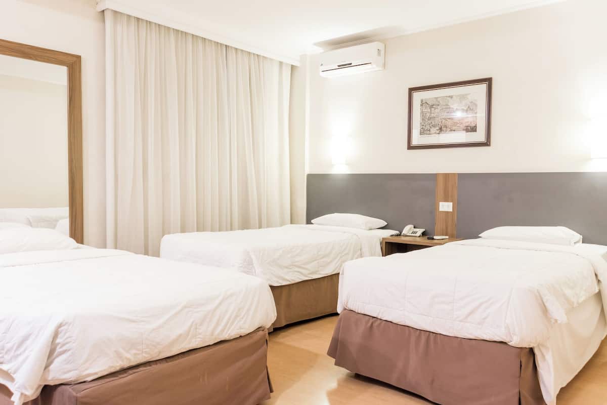 Una habitación de hotel con tres camas, un espejo grande, un cuadro en la pared y un equipo de aire acondicionado.