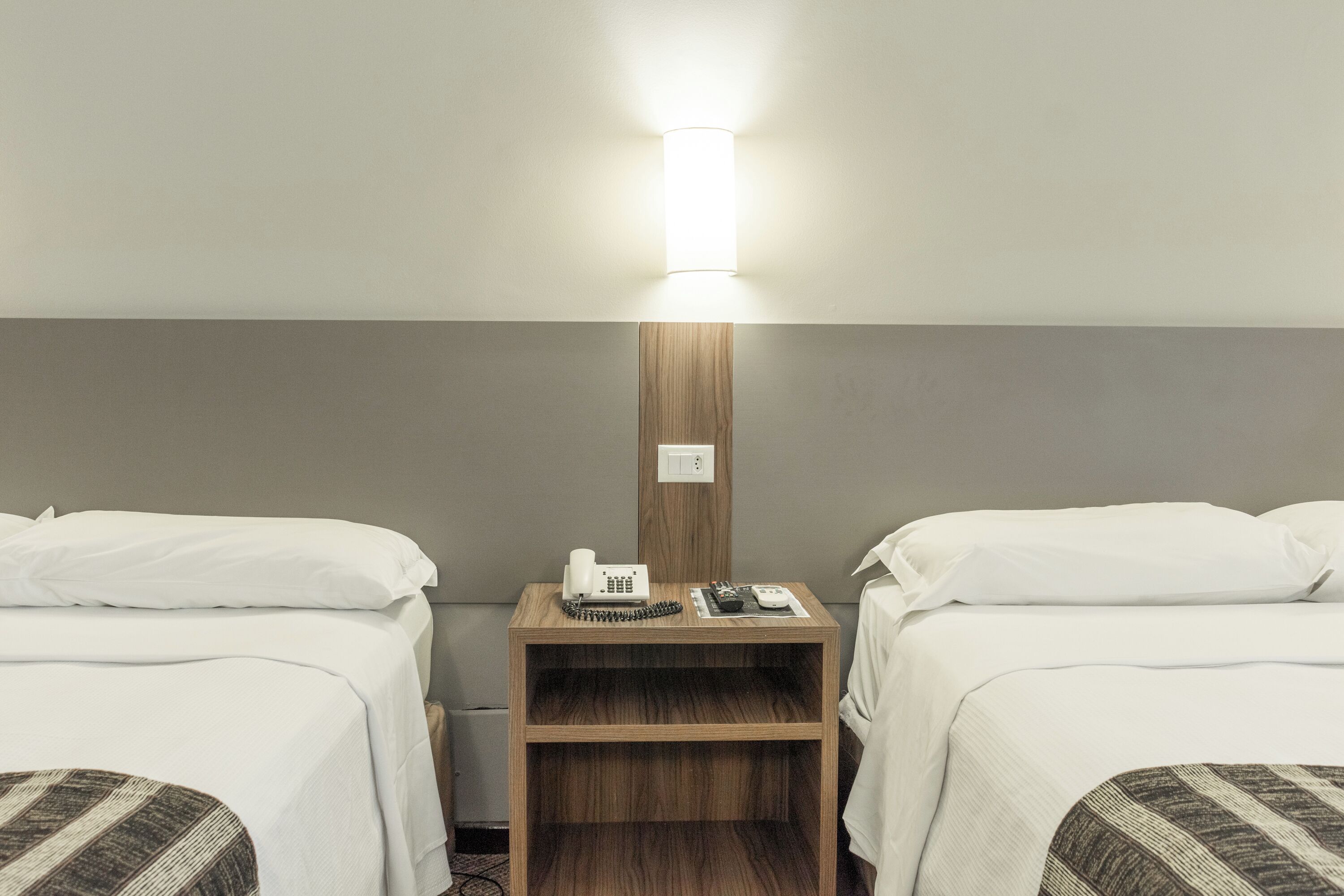 A hotel room with two single beds, a wooden nightstand with a lamp, a telephone, and a small table.
