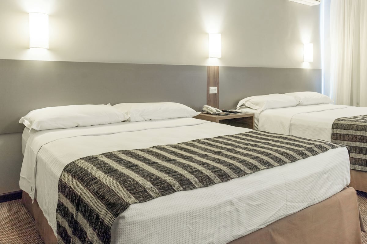 Habitación de hotel con dos camas, cada una con ropa blanca y un plaid a rayas. Hay lámparas de noche y un teléfono en la mesita de noche.