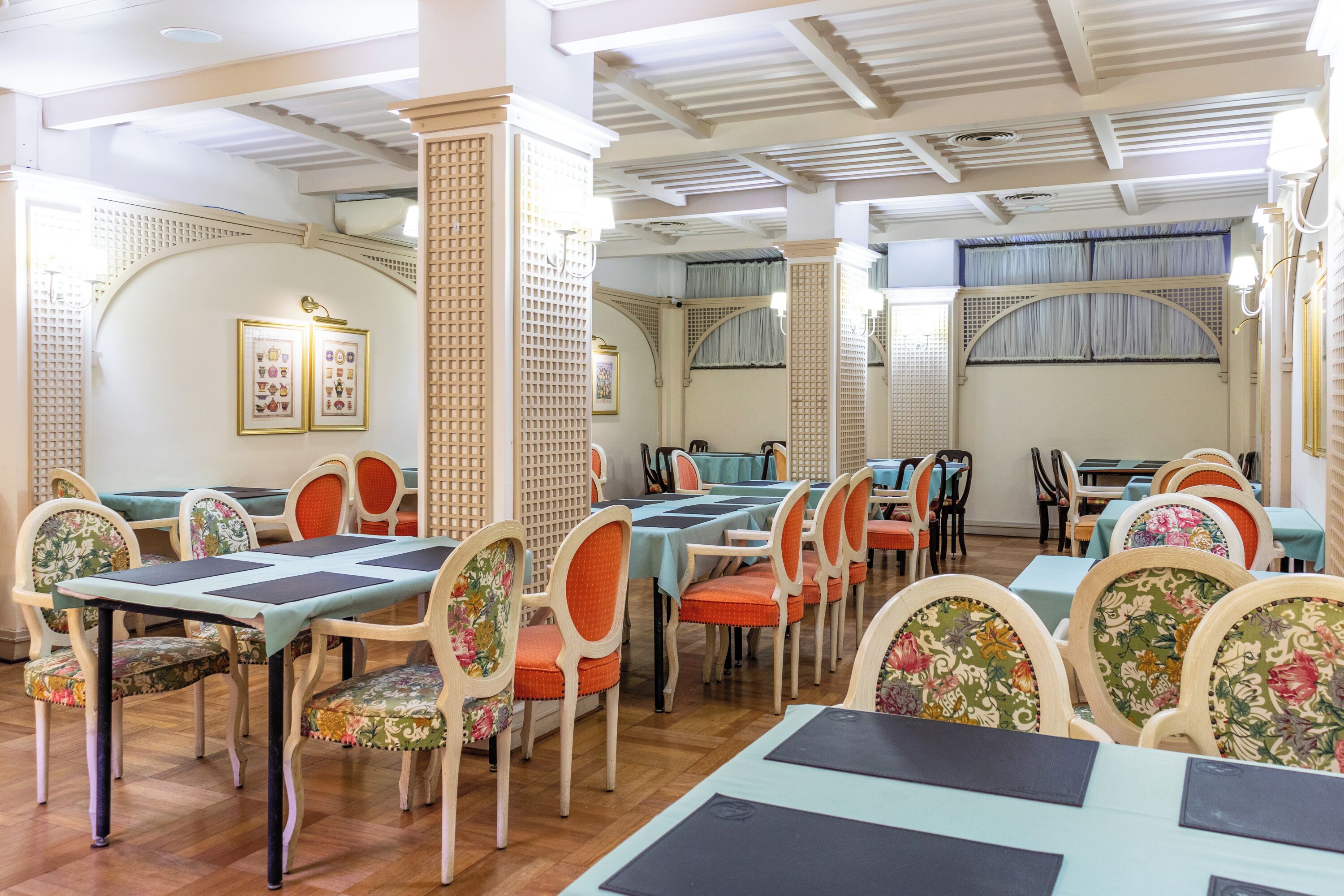 A dining area with tables and chairs, wooden floors, and decorative wall panels.