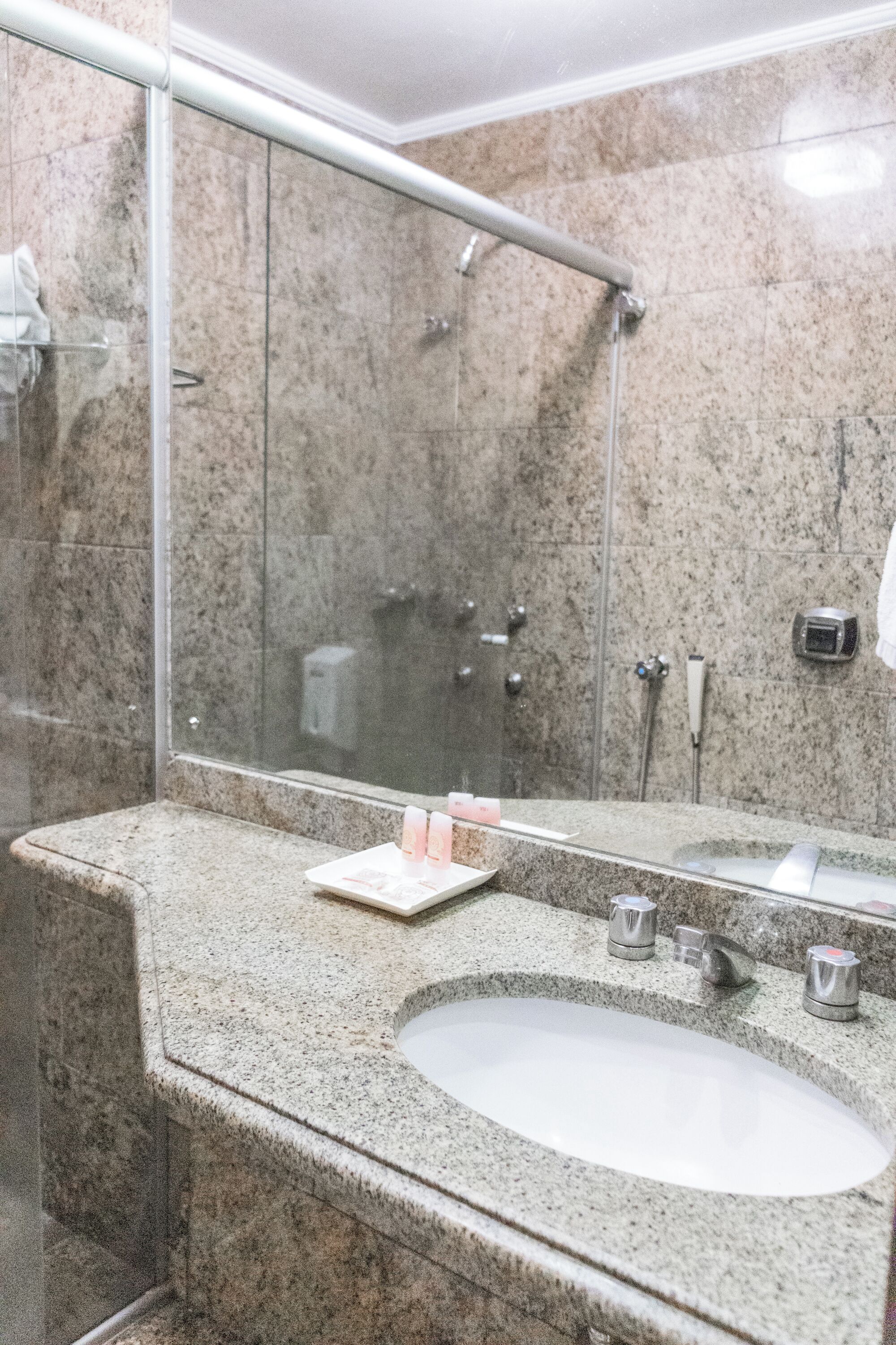 A bathroom with a granite countertop, a sink, a mirror, and a shower area.
