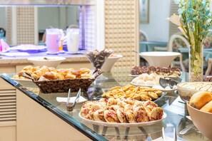 A buffet with various food items including pastries, desserts, and a floral arrangement. - Hotel Lancaster (Curitiba)