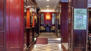 Eine Hotelhalle mit Marmorboden, Holzvertäfelung, einer Rezeption und einem an der Wand befestigten Schild, das Einrichtungen wie eine Lobbybar und ein Restaurant auflistet.