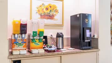 Uma estação de café com vários dispensadores de bebidas, uma cafeteira e uma lata de lixo.