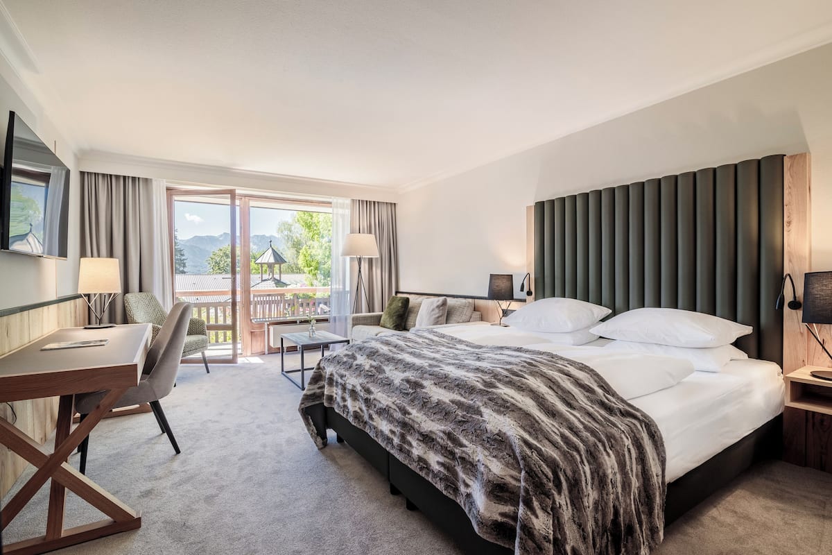A hotel room with a bed, desk, chair, and a view of the outdoors.