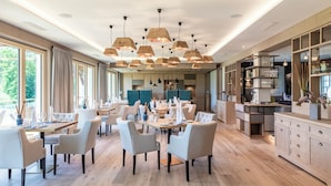 Uma sala de jantar moderna com mesas de madeira, cadeiras brancas e iluminação pendente.