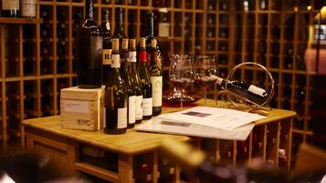 A wooden table with wine bottles and glasses, surrounded by a wine rack in the background.
