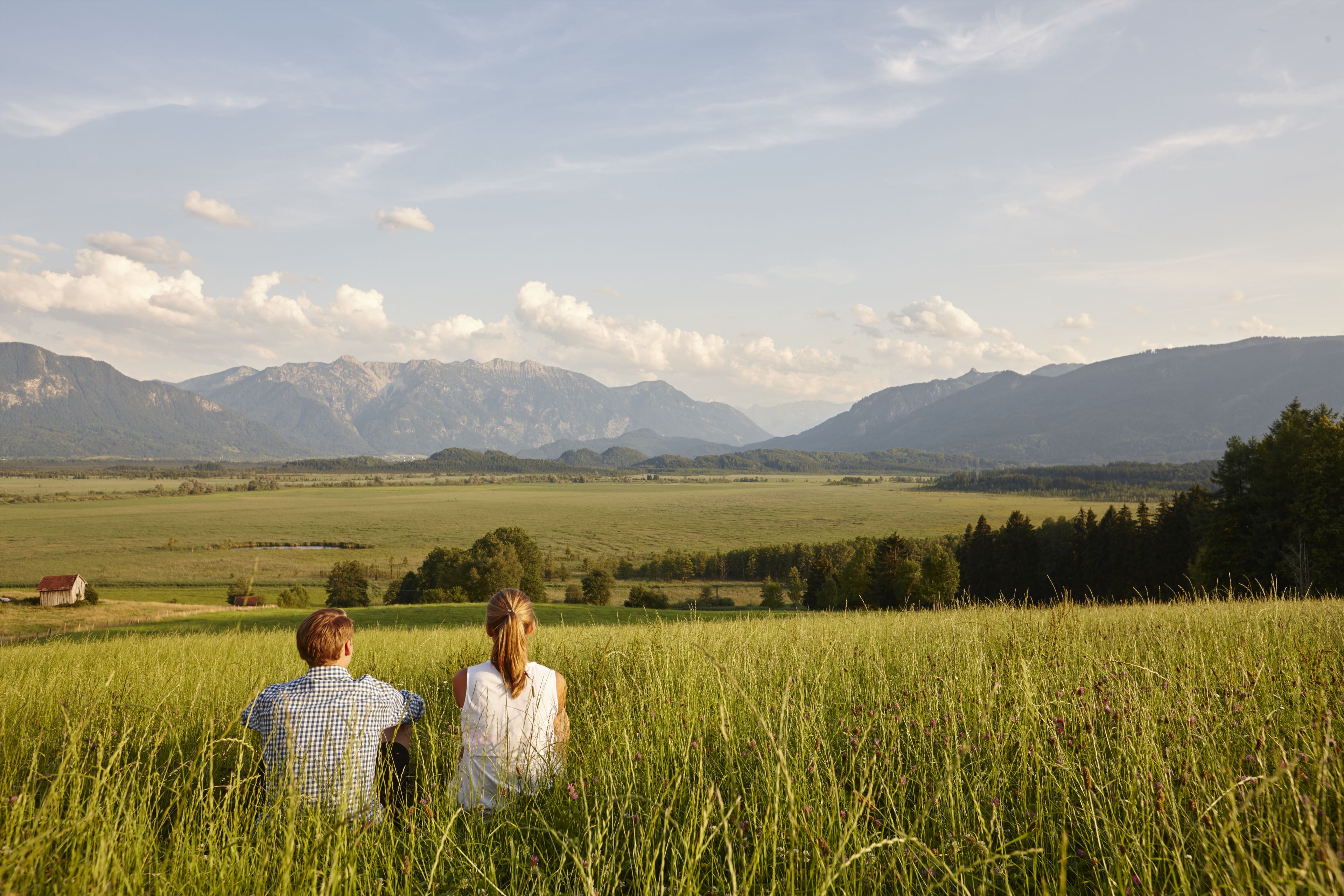 A couple sitting in a field with mountains in the background.