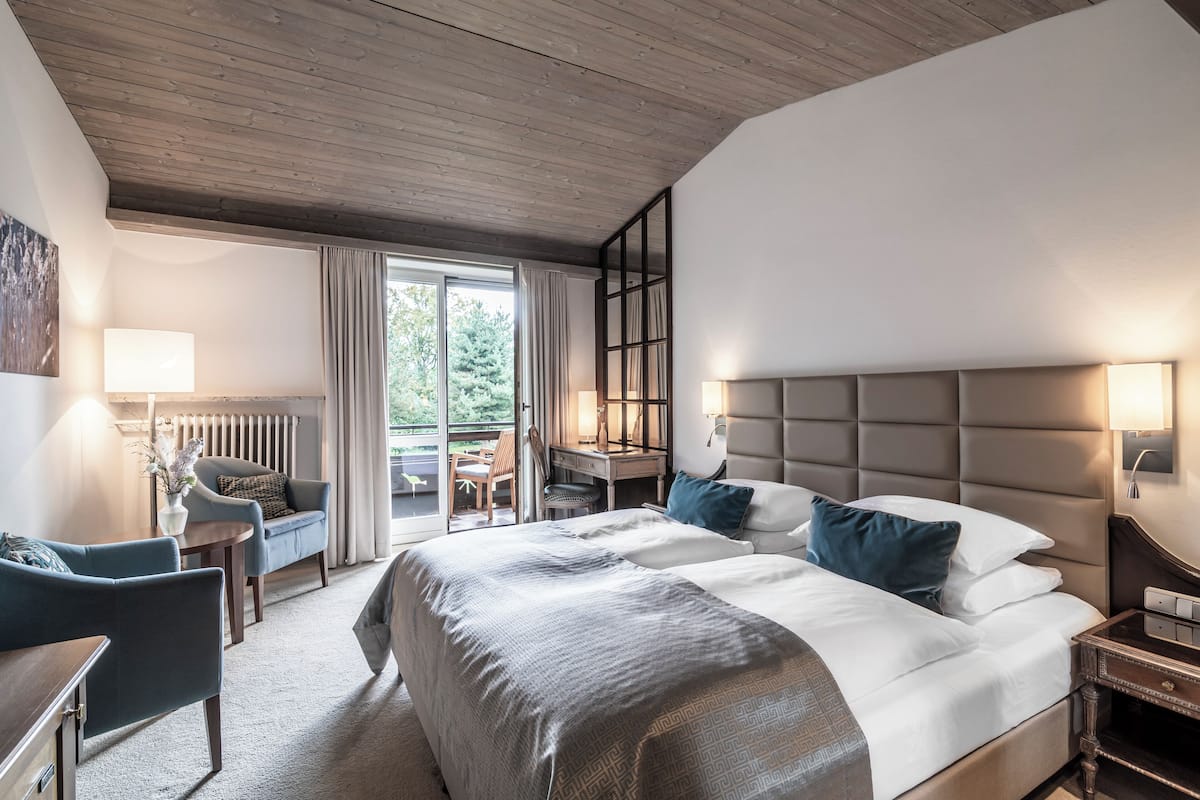 A modern hotel room with a large bed, a desk, a chair, and a view of the outdoors.