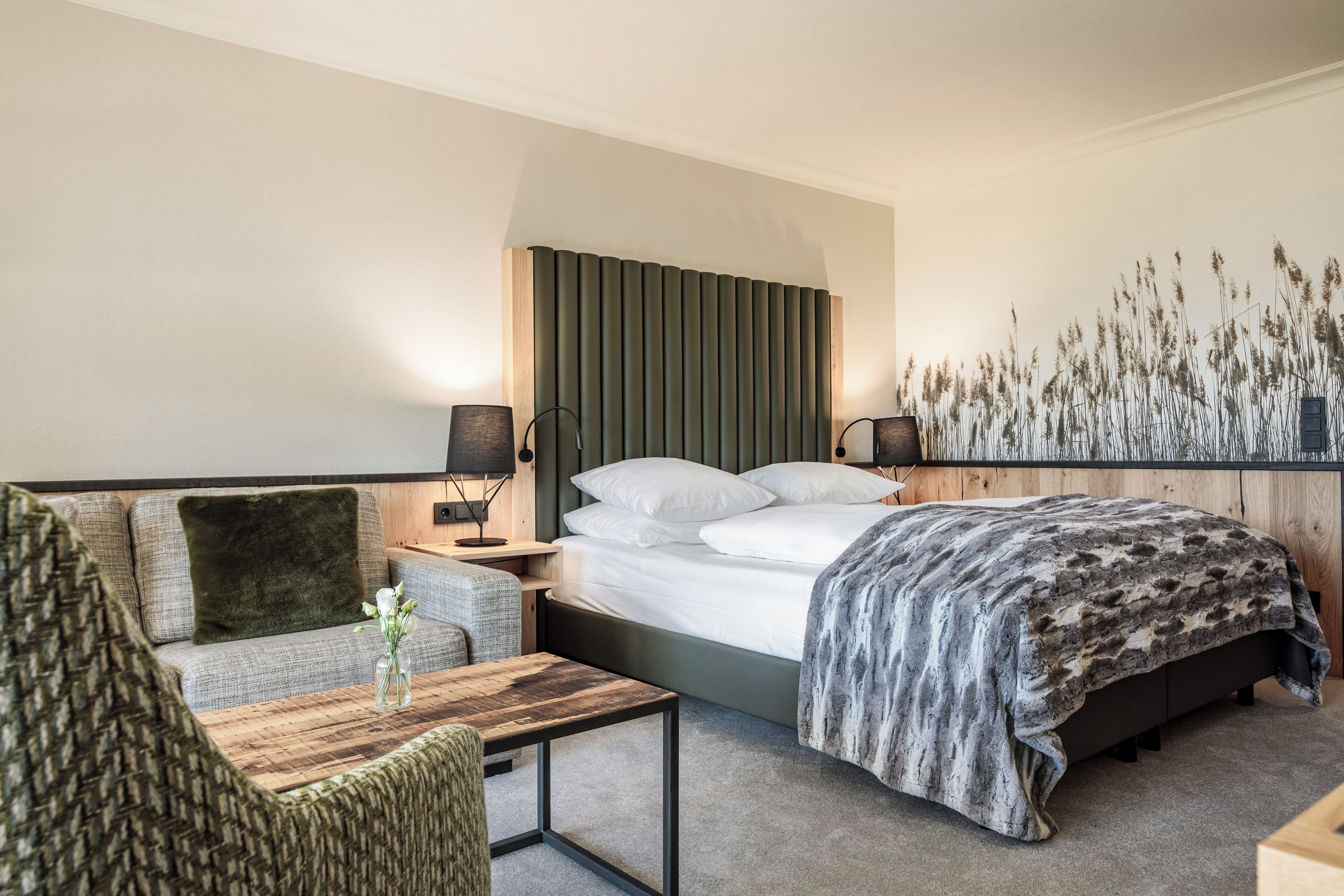 Ein modernes Hotelzimmer mit Bett, Sofa, Couchtisch aus Holz und Nachttisch mit Lampen.