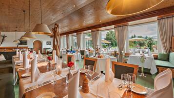 Un restaurant doté d’un plafond en bois et de tables dressées pour le service, de grandes fenêtres et offrant une vue sur l’extérieur.