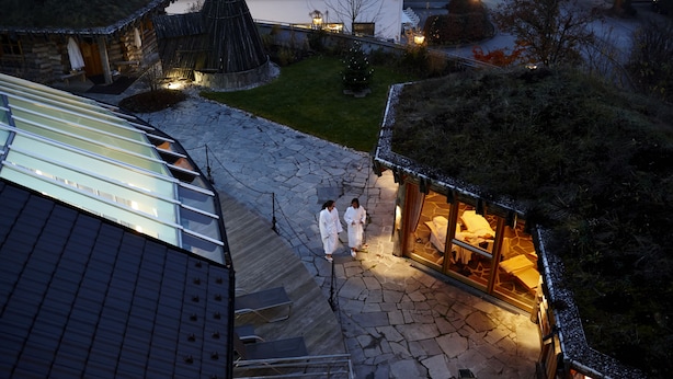 Um pátio com calçamento de pedra, um edifício com cobertura de vidro, uma estrutura de madeira com telhado de palha e um pinheiro de Natal.