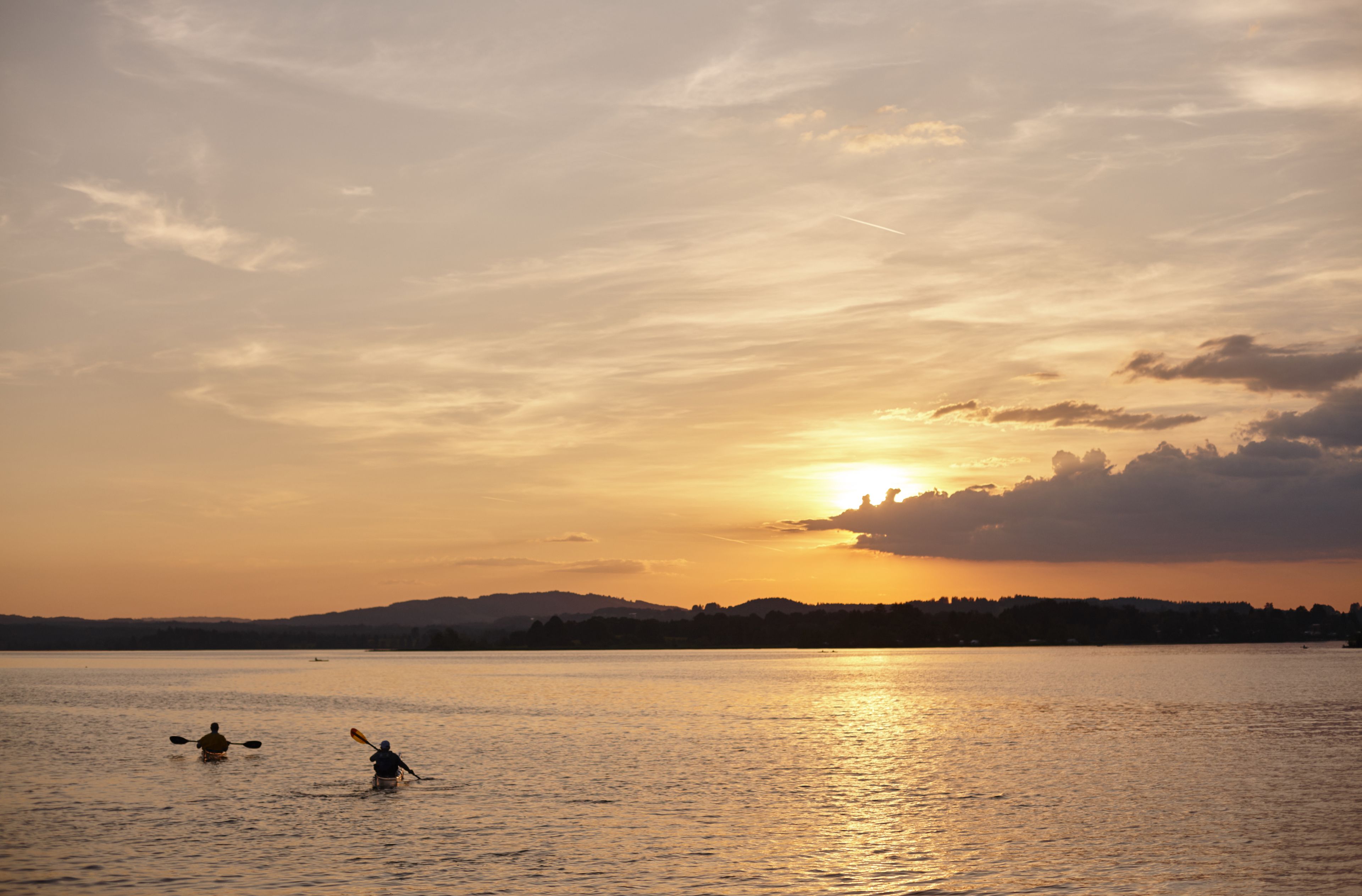 Ein Sonnenuntergang über einem stillen See, auf dem Menschen mit Kanus fahren.