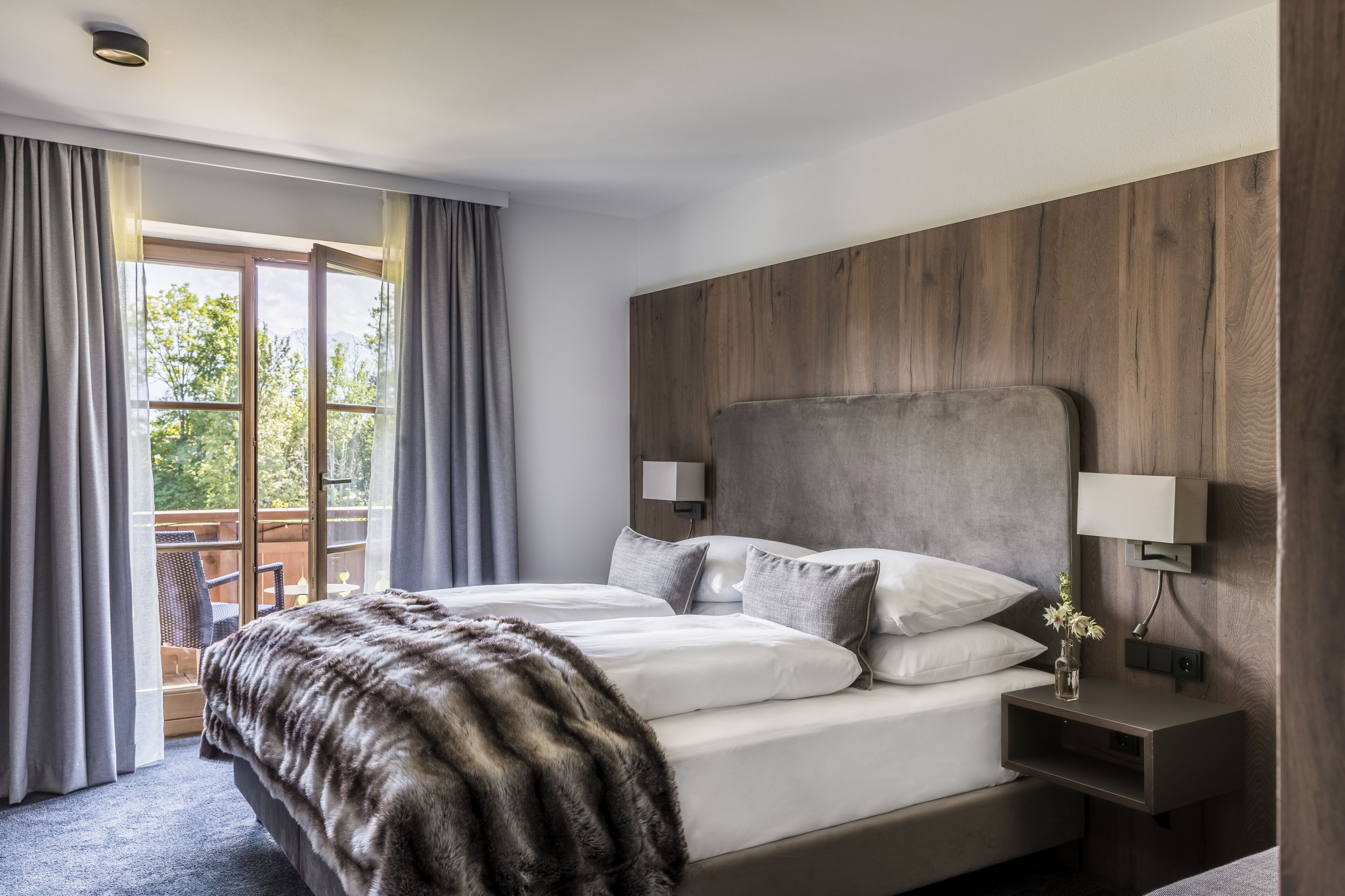 Une chambre d’hôtel moderne avec un grand lit, une tête de lit en bois et un balcon agrémenté de rideaux.