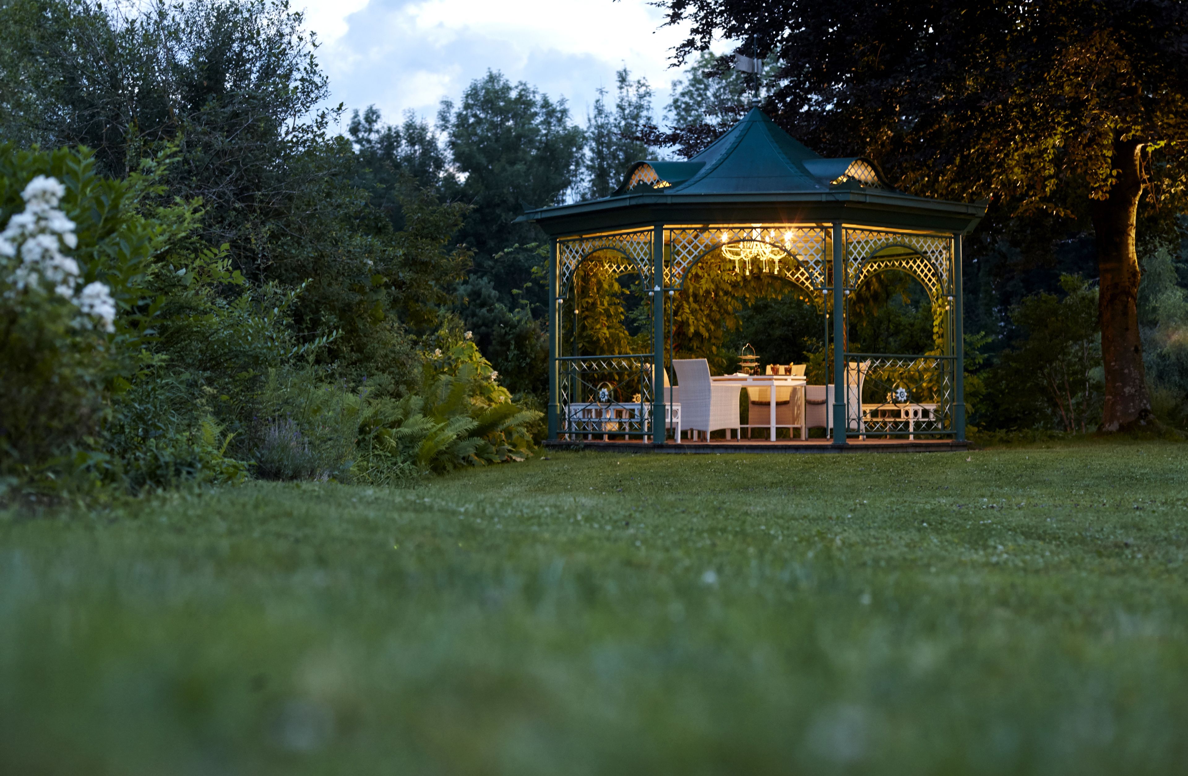 A gazebo with a glass roof, surrounded by lush greenery.